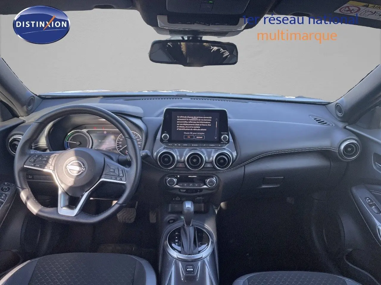 Vue frontale de l'habitacle du Nissan Juke gris, avec tableau de bord numérique et écran tactile central.
