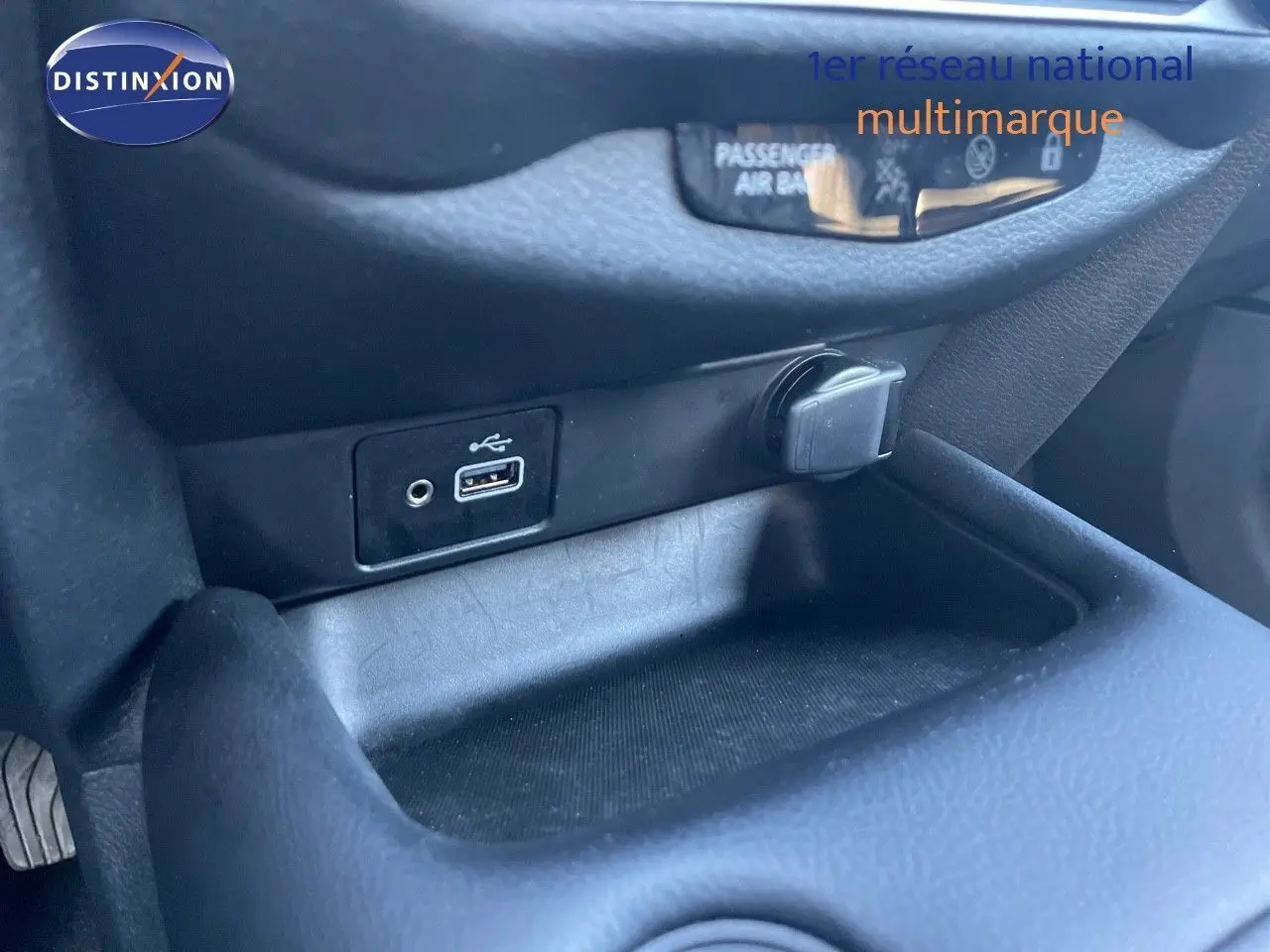 Prise USB et allume-cigare dans le rangement central du Nissan Juke 2024 gris squale métal, intérieur noir.