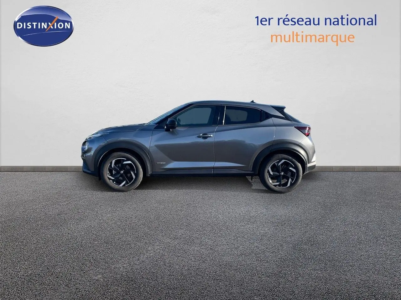 Profil côté gauche du Nissan Juke 1.6 HEV gris squale métal 2024, avec jantes noires et toit noir contrasté.