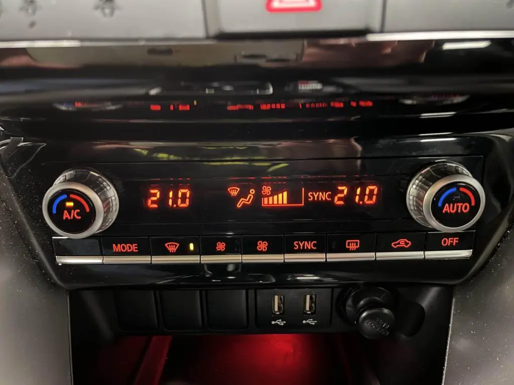 Panneau de climatisation automatique bi-zone rouge éclairé du Mitsubishi Eclipse Cross gris, avec commandes et prises USB visibles.
