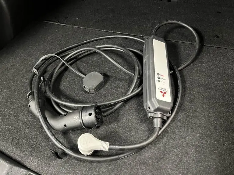 Câble de recharge noir Mitsubishi pour Eclipse Cross hybride rechargeable, posé sur un fond gris foncé.