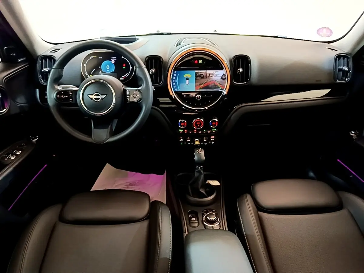 Vue intérieure frontale du tableau de bord et volant cuir noir du MINI COUNTRYMAN Cooper SE 2023 avec écran tactile central rond.