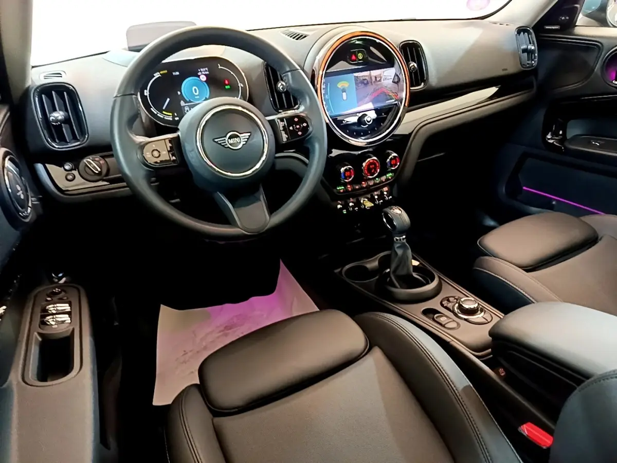 Intérieur avant droit du MINI Countryman vert 2023, volant cuir, écran tactile rond et éclairage d’ambiance violet.