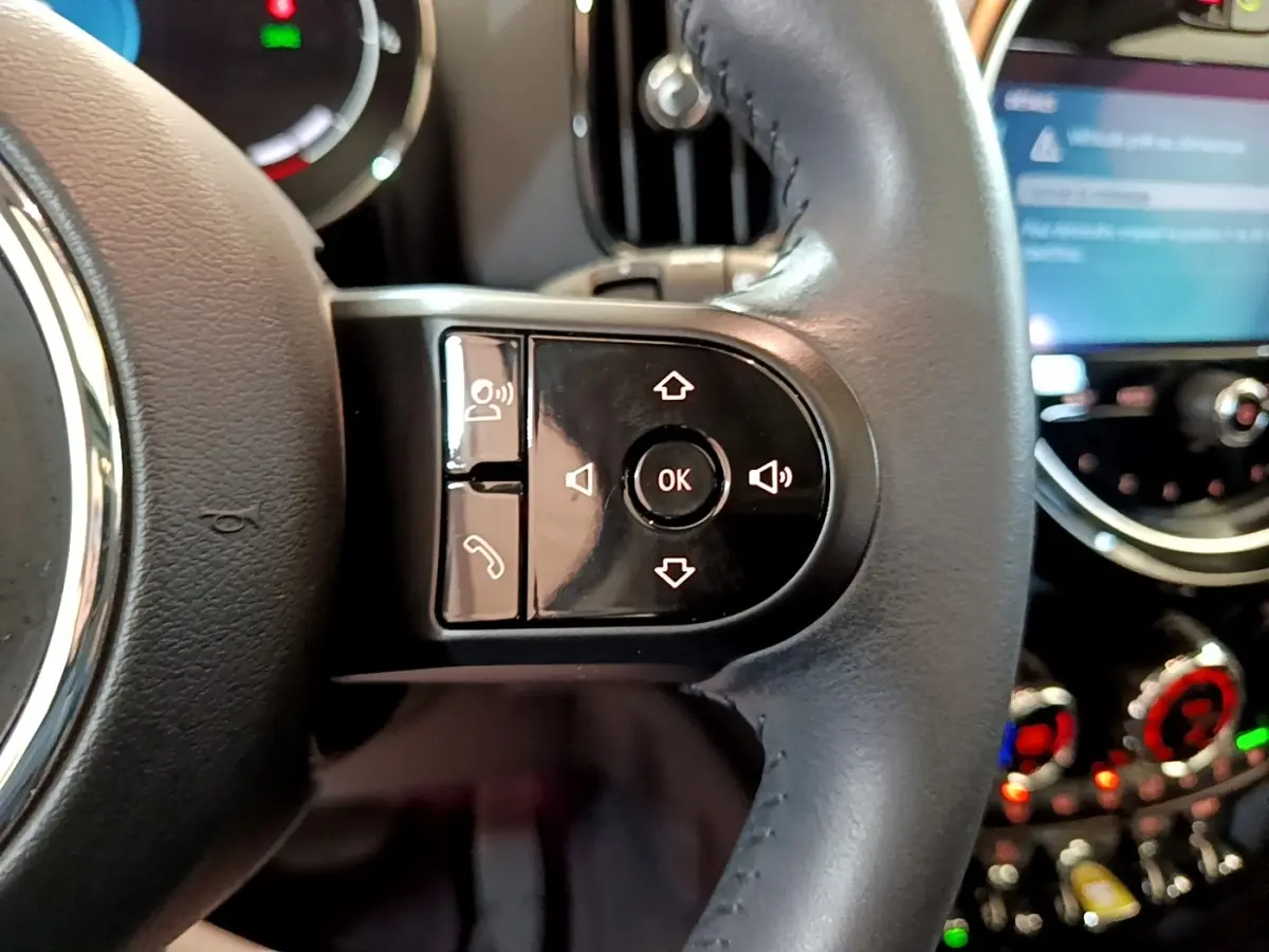 Gros plan sur les commandes du volant cuir noir du MINI COUNTRYMAN 2023, avec écran tactile flou en arrière-plan.