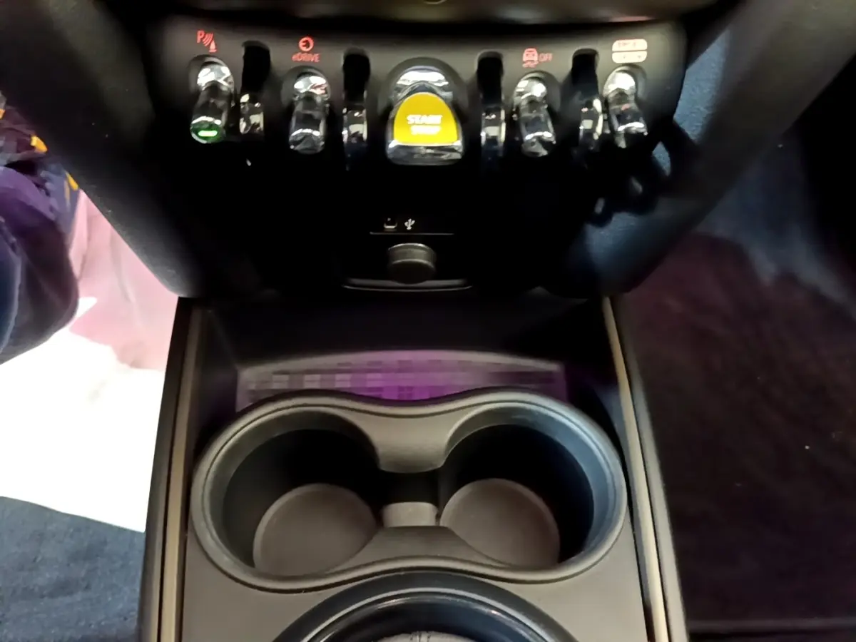 Gros plan sur la console centrale noire du MINI Countryman 2023 avec boutons de commande et bouton start/stop jaune.