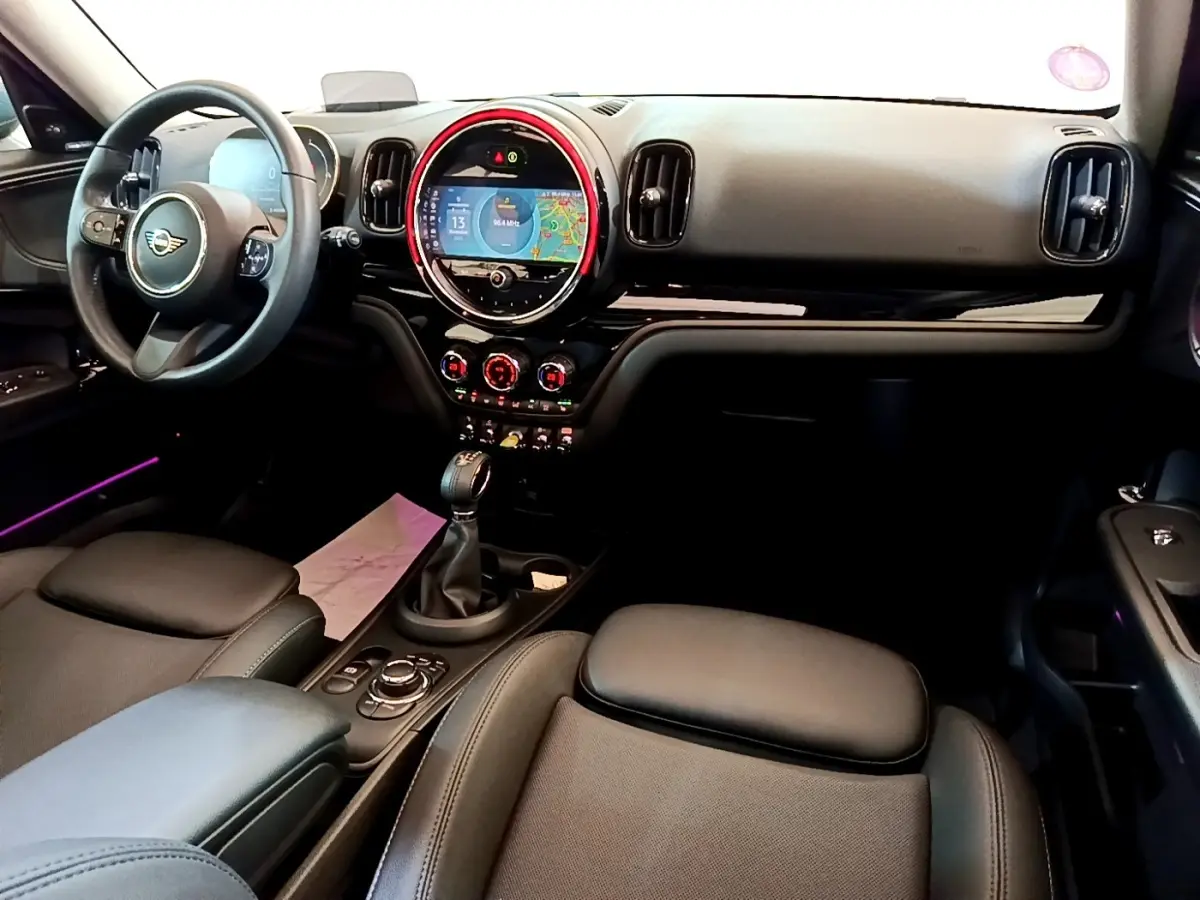 Intérieur avant du MINI Countryman Cooper SE 2023, tableau de bord noir avec écran tactile circulaire et éclairage d'ambiance rouge.