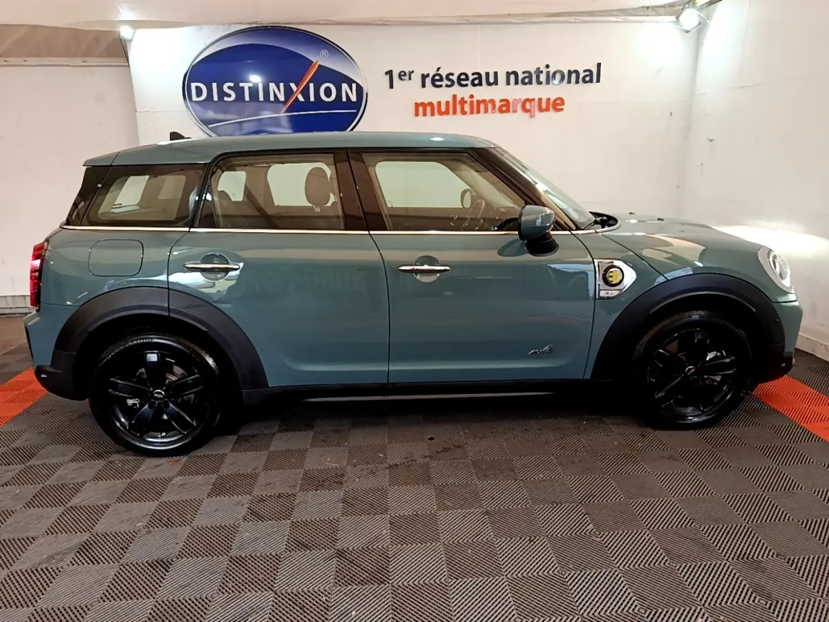 Profil côté gauche d'un MINI Countryman hybride rechargeable vert avec toit blanc et jantes noires brillantes.