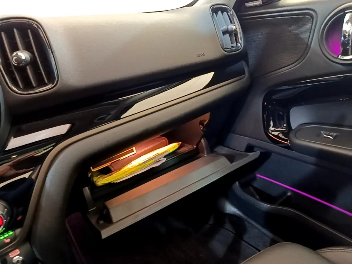 Intérieur MINI Countryman Cooper SE 2023, vue du côté passager avec boîte à gants ouverte et éclairage d’ambiance violet.