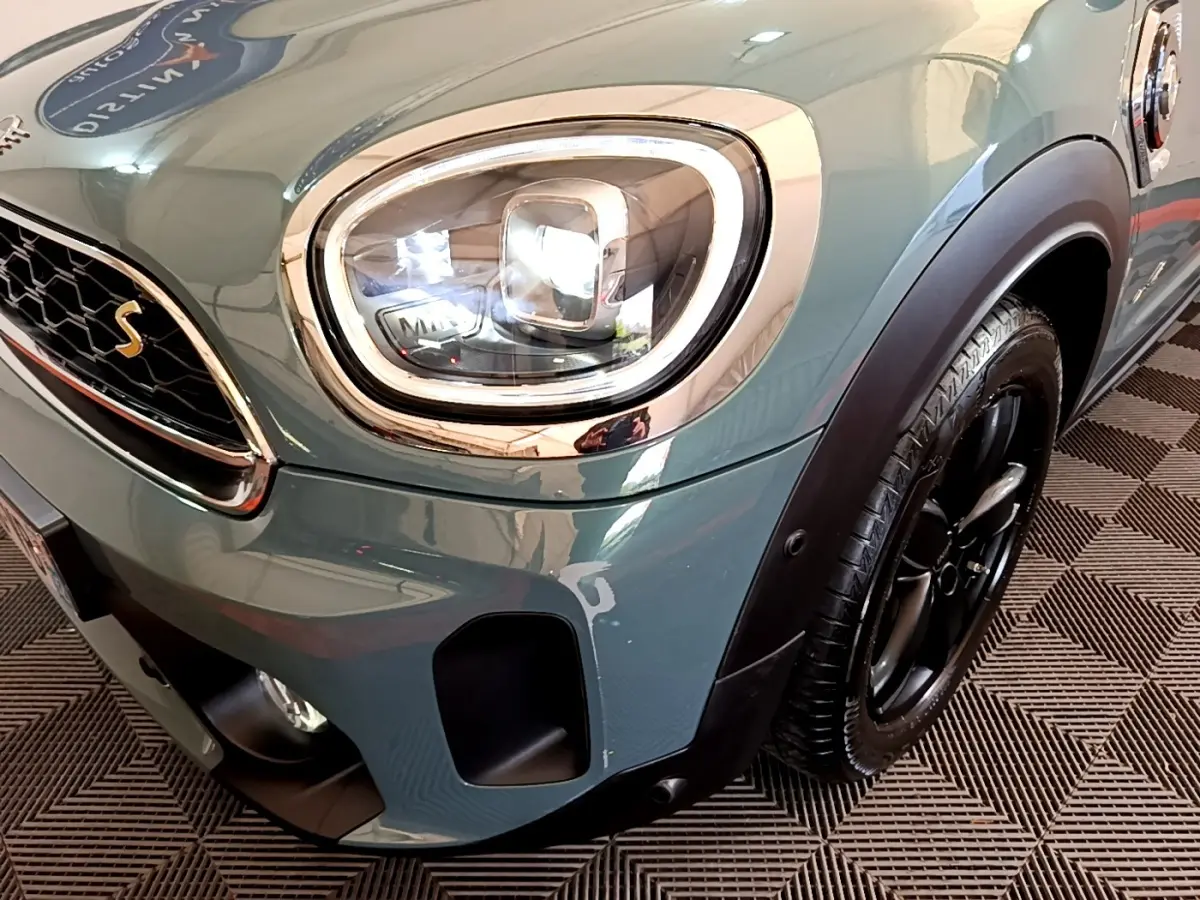 Gros plan sur le phare avant gauche et la roue noire d'une MINI Countryman Cooper SE vert métallisé.