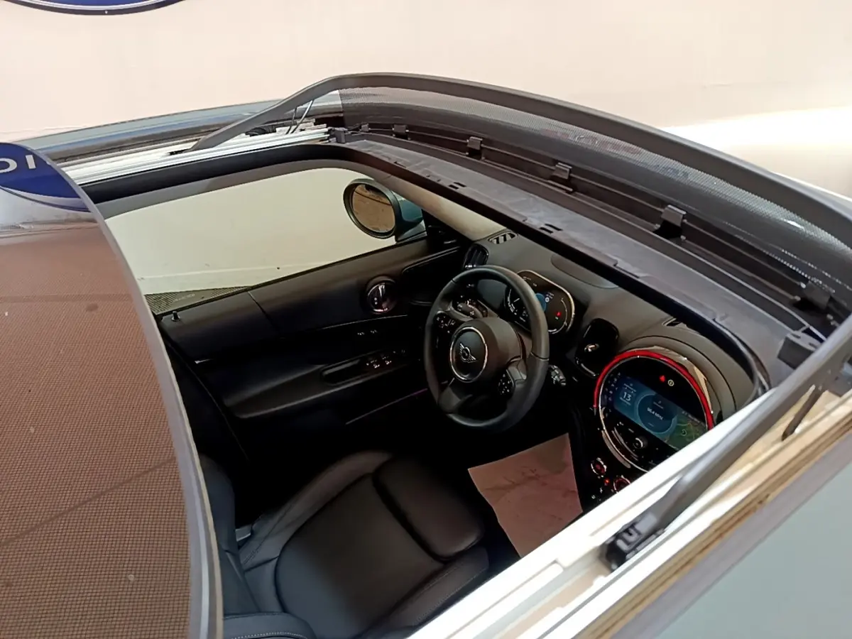 Vue intérieure du tableau de bord et volant cuir noir d'une MINI Countryman hybride rechargeable 2023, toit ouvrant ouvert.