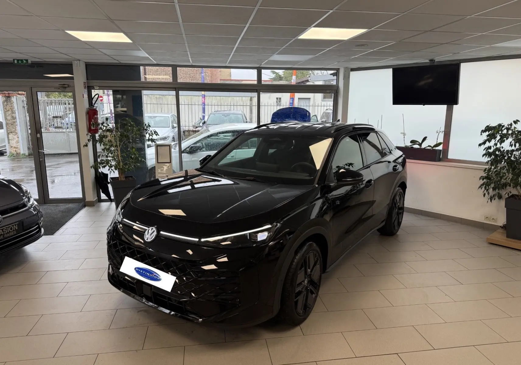 Volkswagen T-Roc Black R-Line noir intense en 3/4 avant droit, intérieur showroom avec jantes noires distinctives.