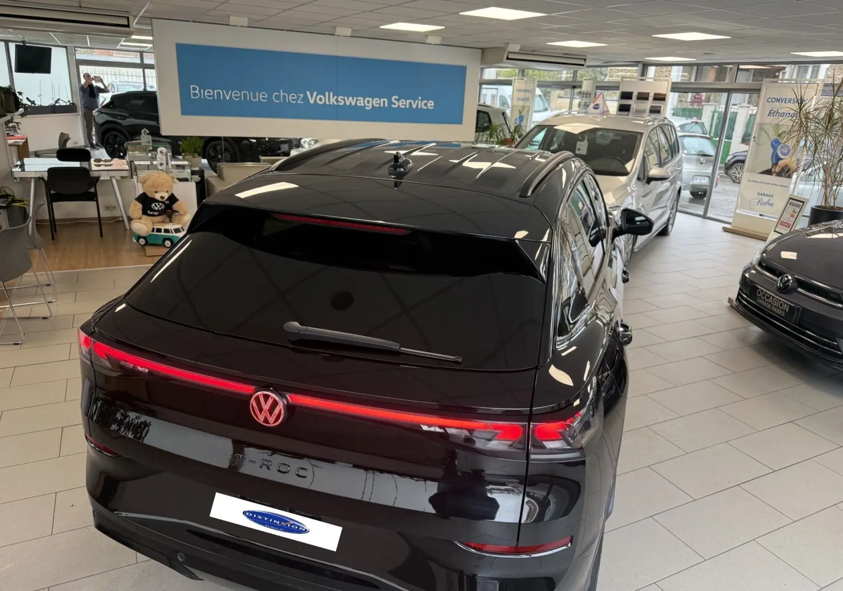 Vue 3/4 arrière du Volkswagen T-Roc noir intense avec feux arrière LED allumés dans un showroom.