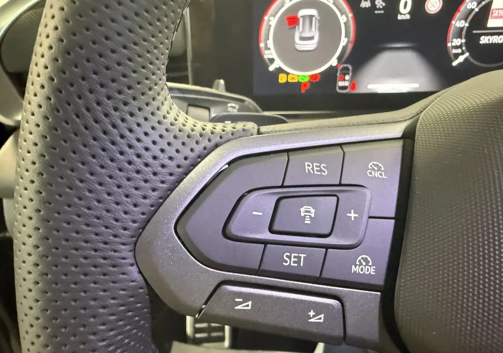 Gros plan sur les commandes de régulateur de vitesse au volant perforé du Volkswagen T-Roc noir intense 2026.