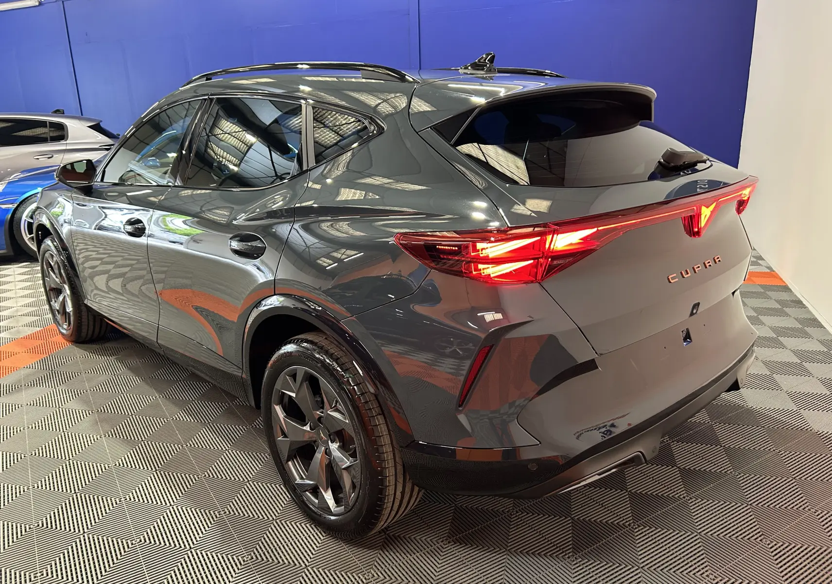 Vue 3/4 arrière droite d’un CUPRA Formentor bleu foncé métallisé avec feux arrière allumés et hayon électrique.