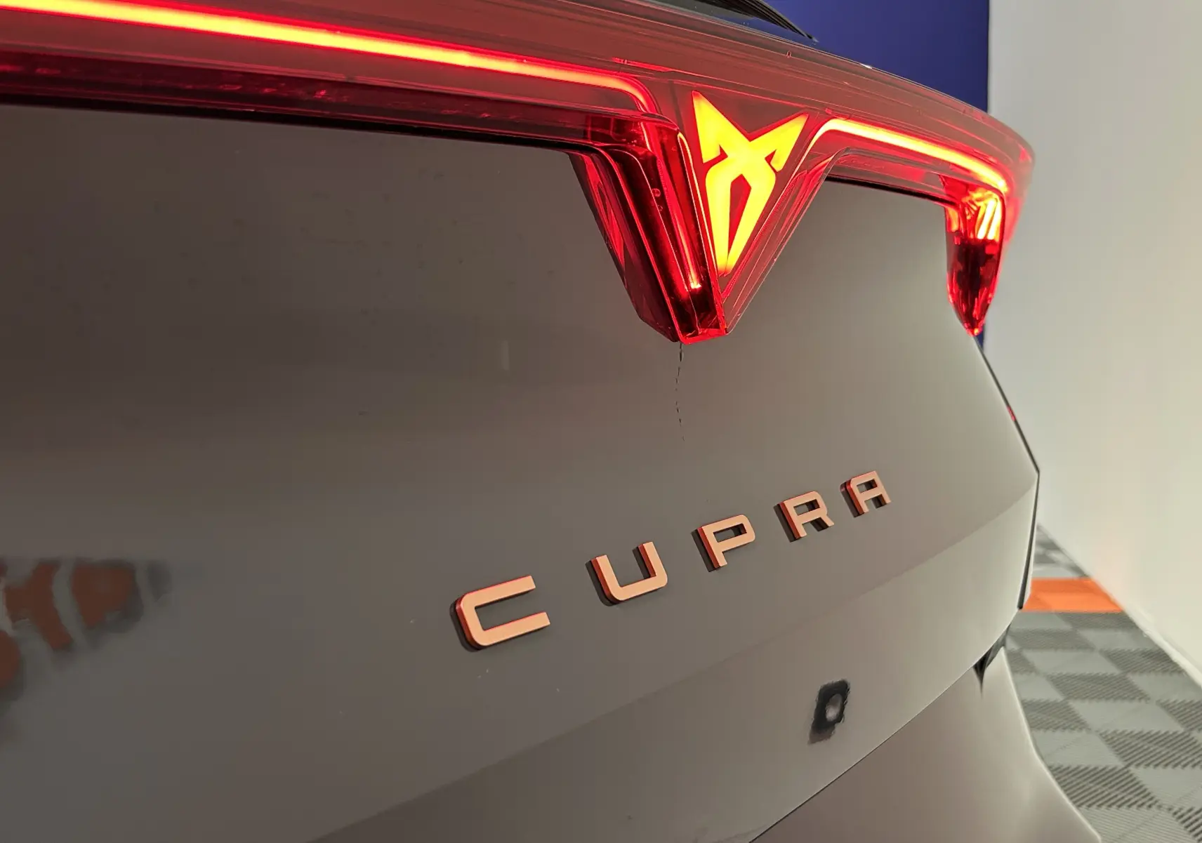 Gros plan sur le hayon arrière bleu fjord métallisé du Cupra Formentor avec feux LED et logo illuminé rouge.