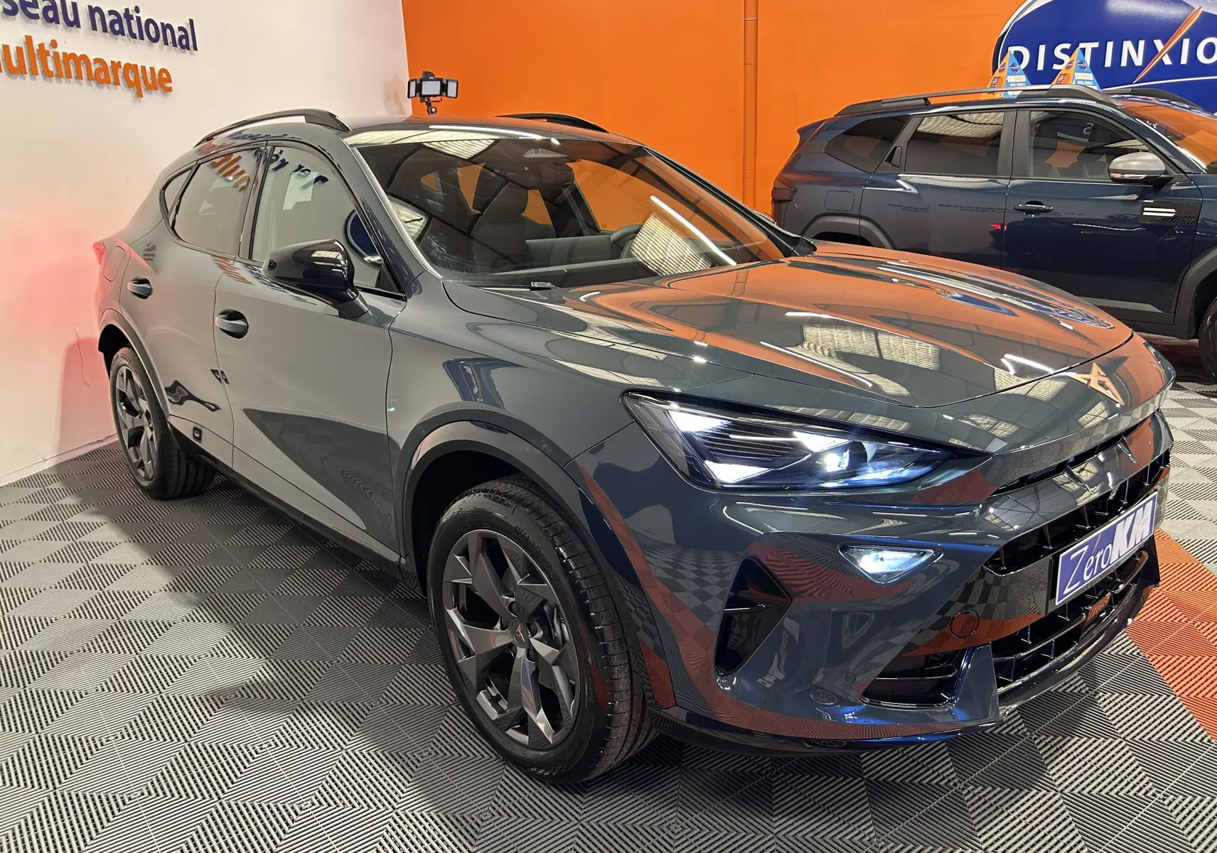 Vue 3/4 avant droit d'une CUPRA Formentor 1.5 eTSI bleu Fjord métallisé avec phares allumés en showroom.