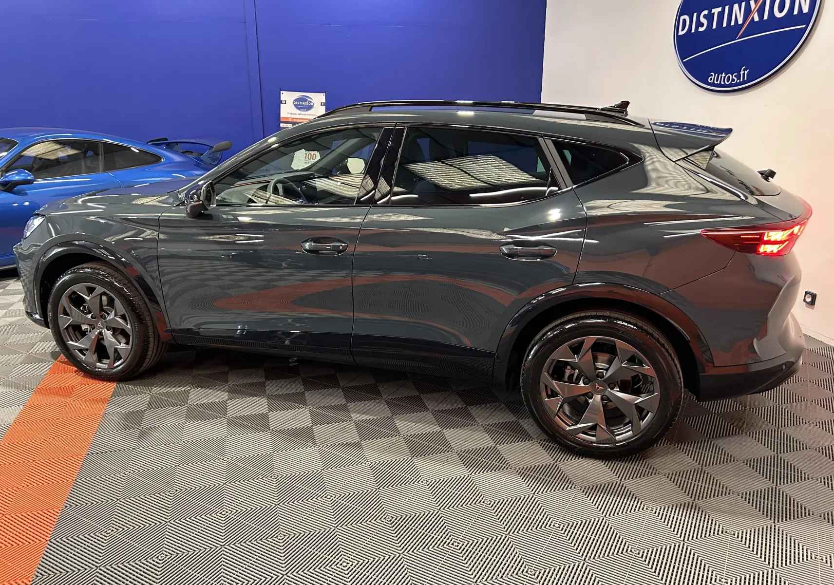 Vue latérale droite du CUPRA Formentor 1.5 eTSI bleu foncé avec jantes alliage et hayon électrique en intérieur showroom.