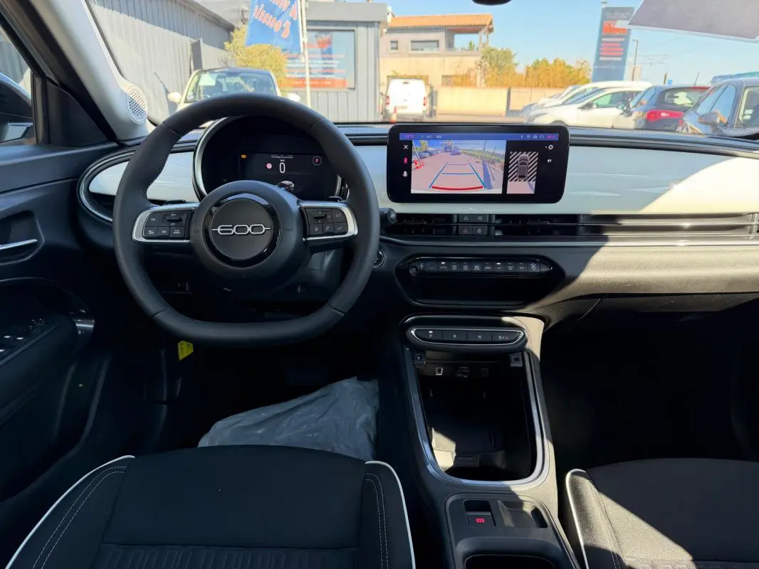 Vue intérieure avant du tableau de bord de la Fiat 600 T-Gen 3 blanc avec écran tactile et volant multifonction.