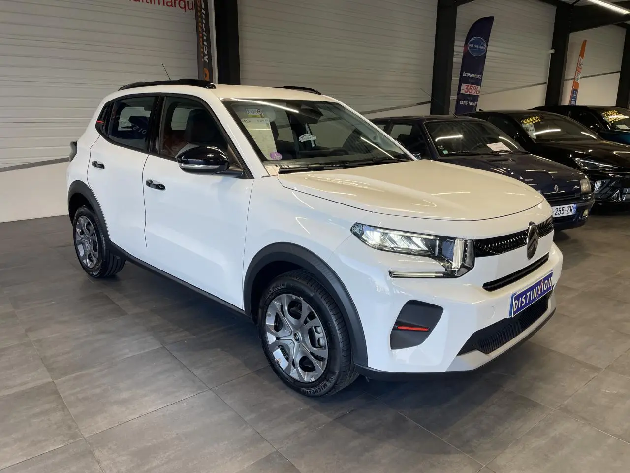 Citroën C3 blanc vue 3/4 avant droit en intérieur avec barres de toit noir brillant et jantes AZURITE.