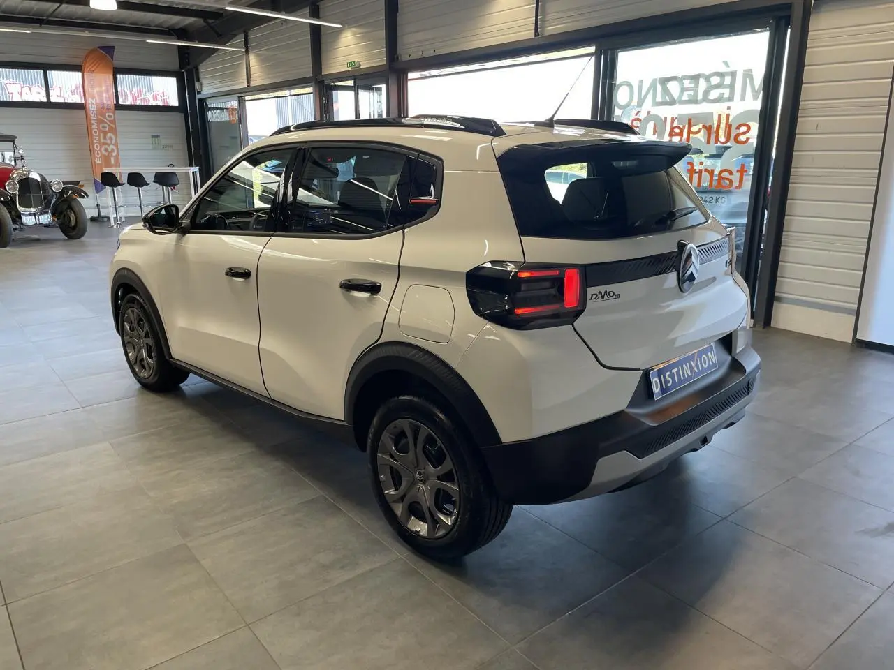 Vue 3/4 arrière droite d'une Citroën C3 blanche avec toit noir et jantes 17 pouces en intérieur showroom.