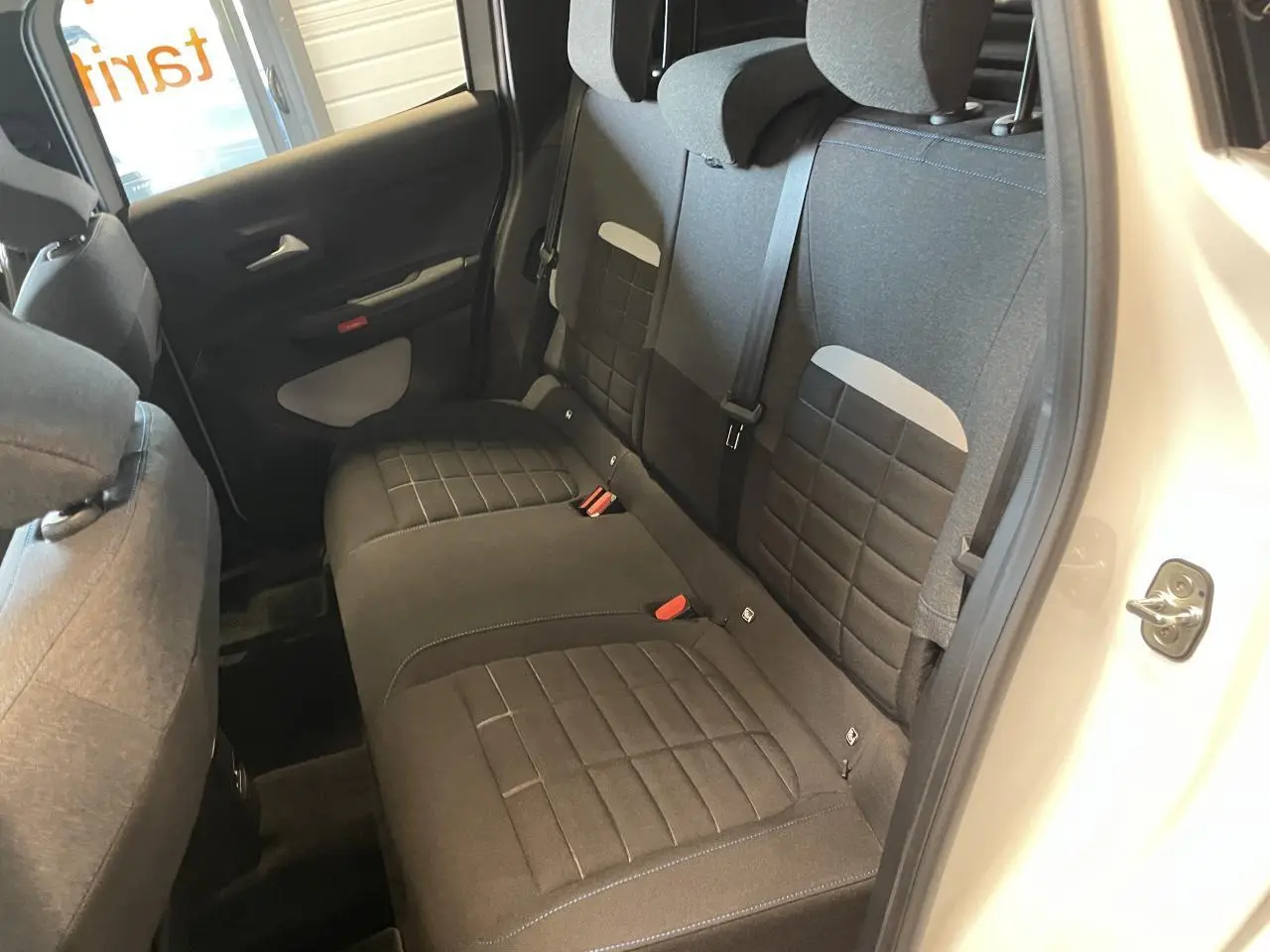 Vue intérieure côté droit sur la banquette arrière tissu noir avec appuie-têtes et ceintures d’une Citroën C3 blanche.