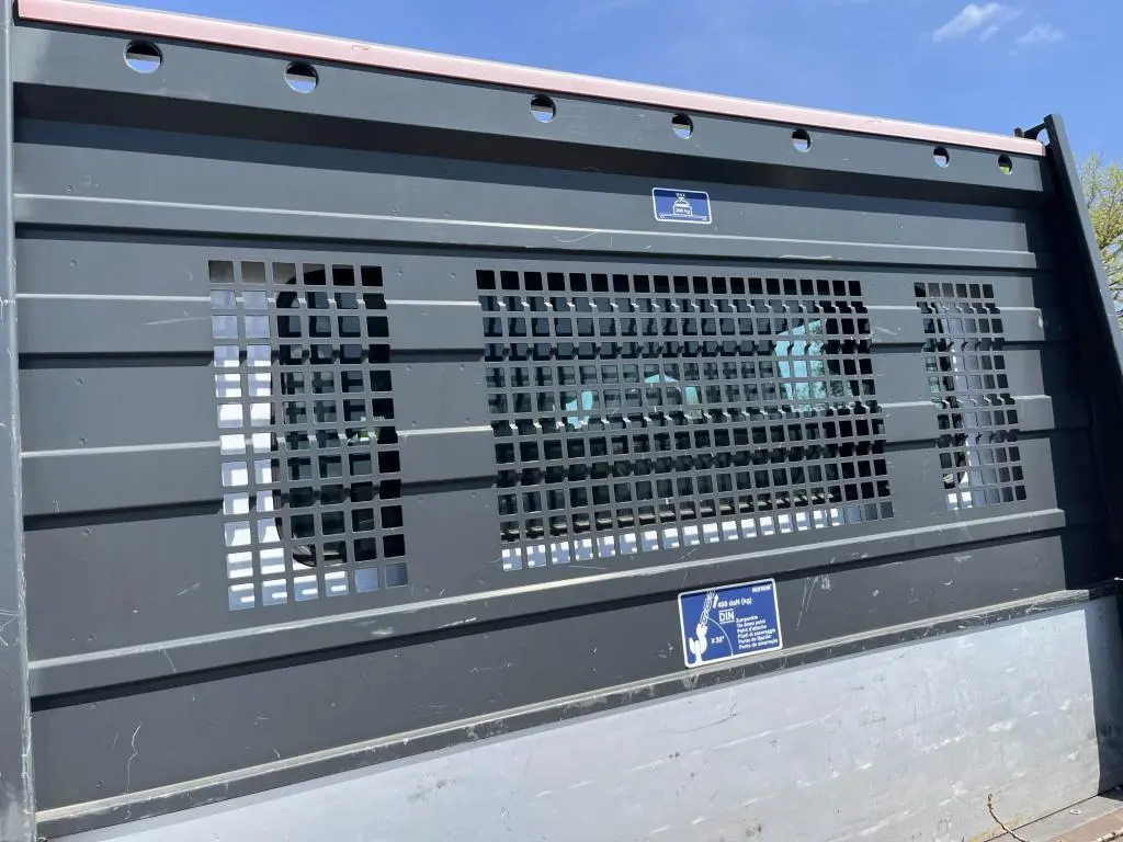 Gros plan sur la grille noire du plateau ridelles aluminium du Renault Master blanc, vue arrière sous ciel bleu.