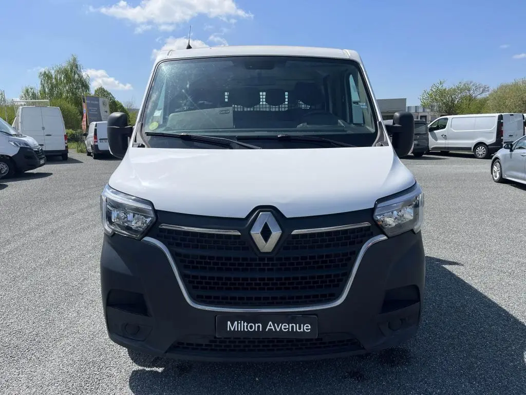 Vue frontale d'un Renault Master blanc avec calandre noire et logo chromé, sur parking ensoleillé.