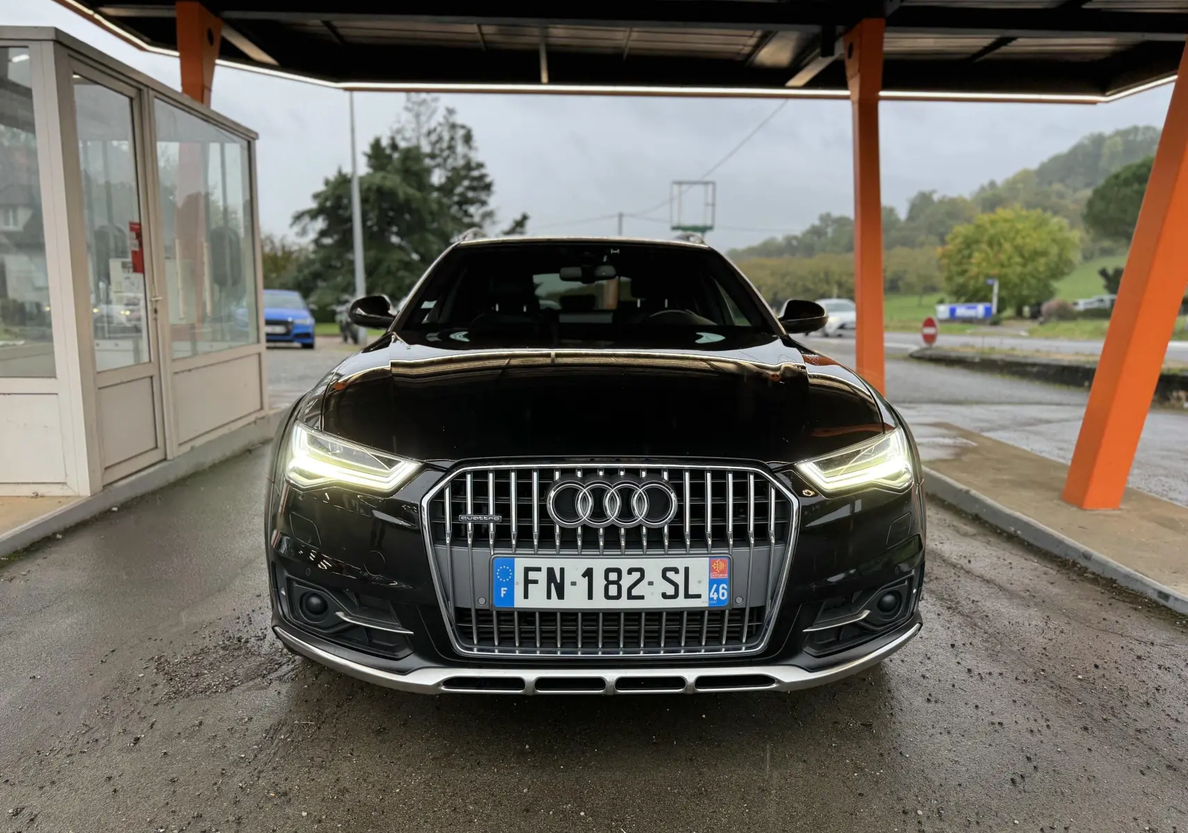 Audi A6 Avant Allroad noire vue de face sous abri, phares LED allumés et calandre chromée distinctive.