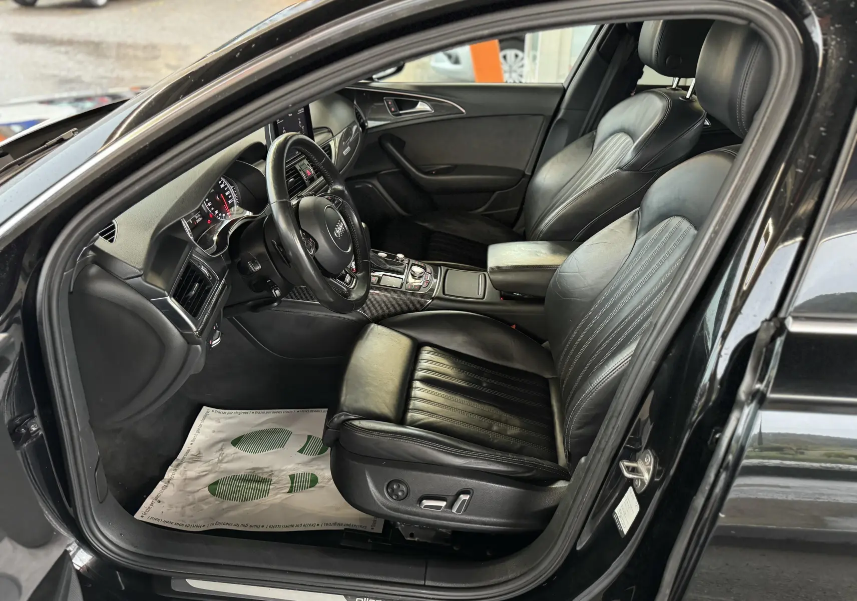 Vue intérieure côté conducteur de l'Audi A6 Avant Allroad noire, sièges cuir noir et tableau de bord moderne.