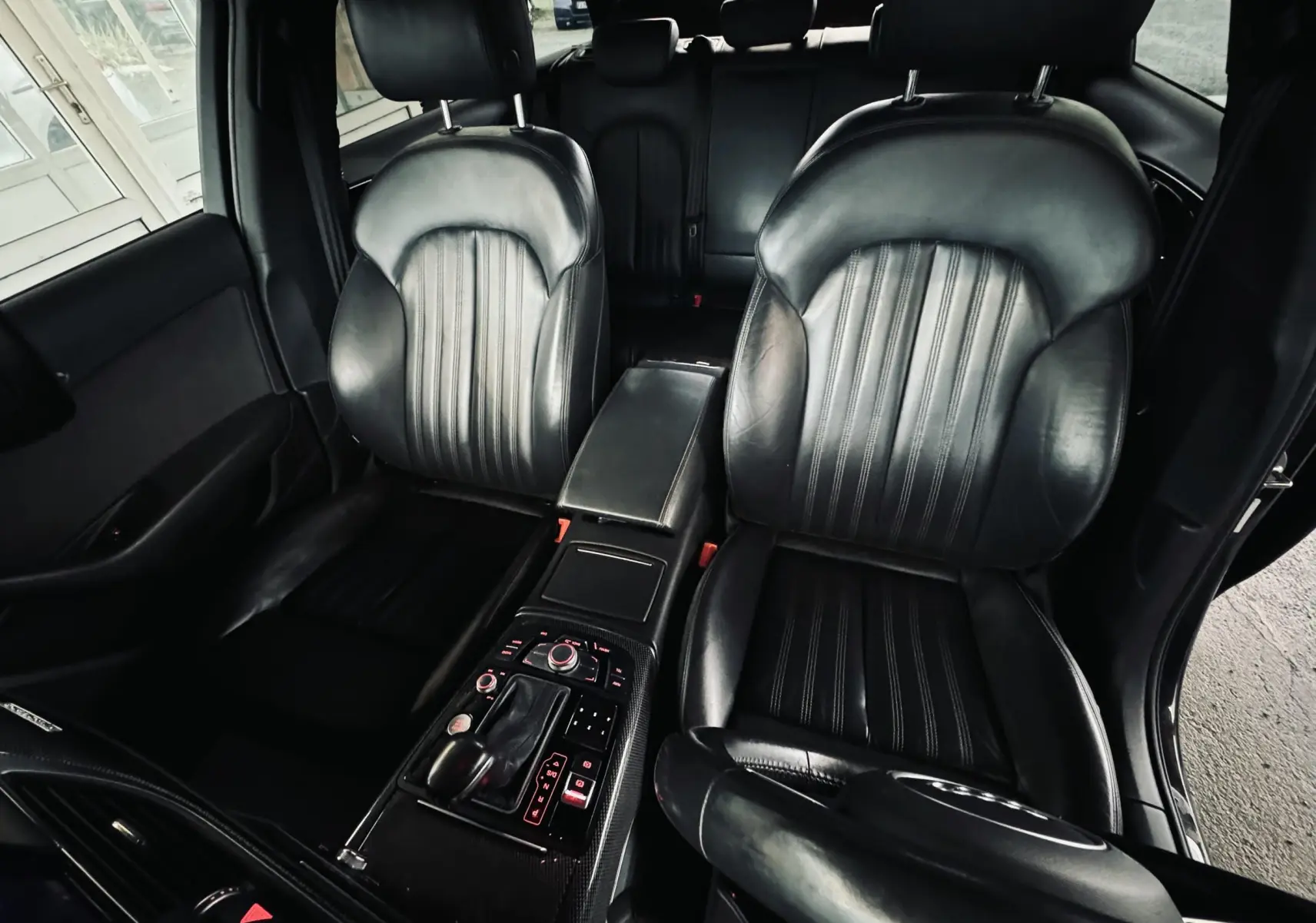 Vue intérieure centrée sur les sièges avant en cuir noir et la console centrale d'une Audi A6 Avant Allroad noire.