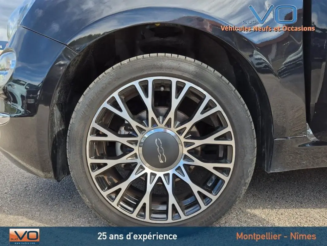 Gros plan sur la roue avant gauche noire d'une FIAT 500C 2024 avec jante alliage et roue de secours visible.