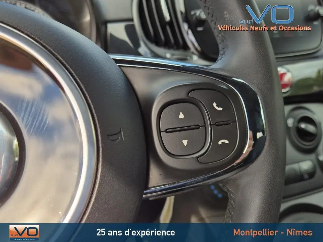 Gros plan sur les commandes du volant noir de la FIAT 500C 2024 hybride essence avec boîte manuelle.