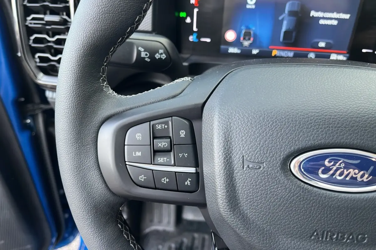 Gros plan sur le volant cuir multifonctions du Ford Ranger 2025 bleu lightning, avec commandes intégrées et tableau de bord numérique visible.
