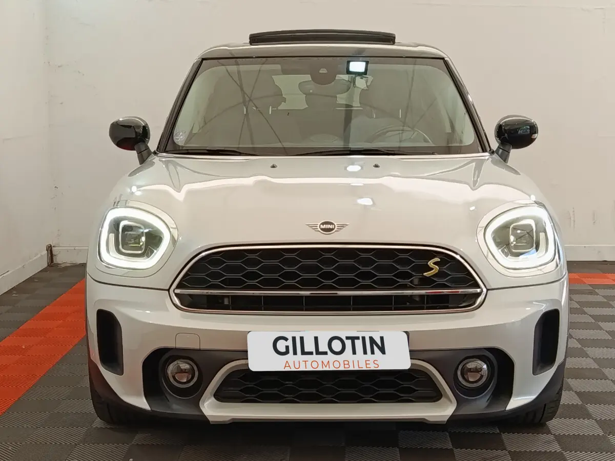 Vue frontale d'une MINI Countryman Cooper SE blanche avec phares LED allumés et calandre noire à motif nid d'abeille.