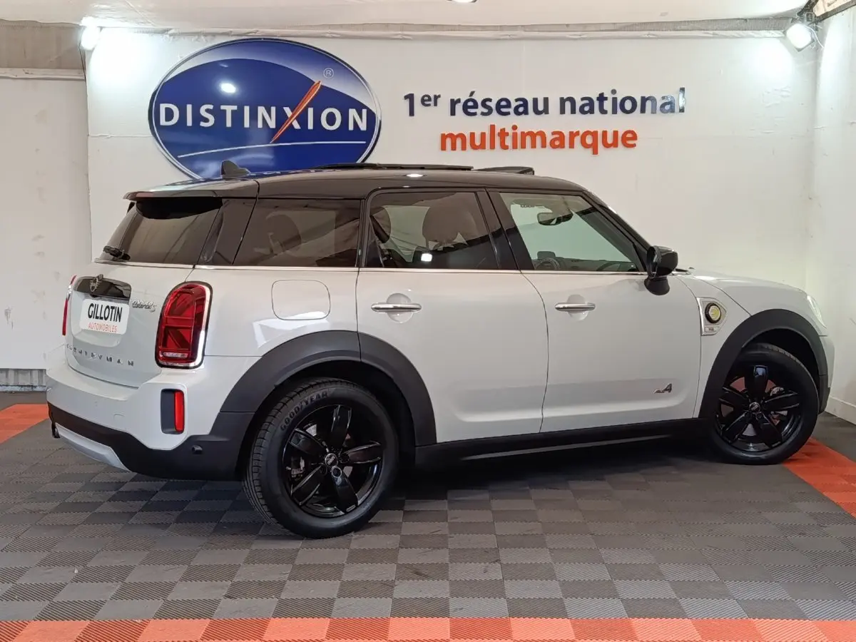 Vue de profil côté gauche d'un MINI Countryman blanc avec toit noir et jantes noires dans un showroom.