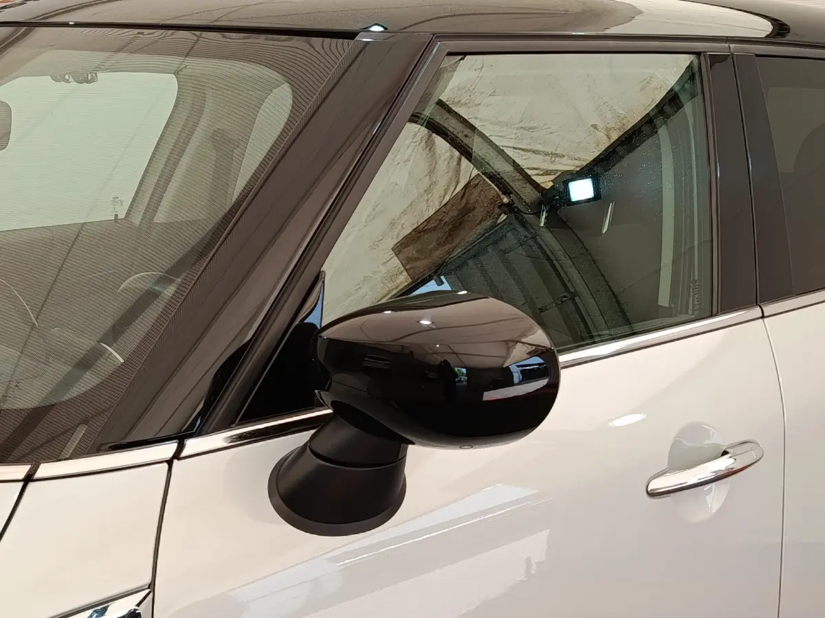 Rétroviseur noir en gros plan côté gauche sur MINI Countryman blanc, avec porte et vitre avant visibles.