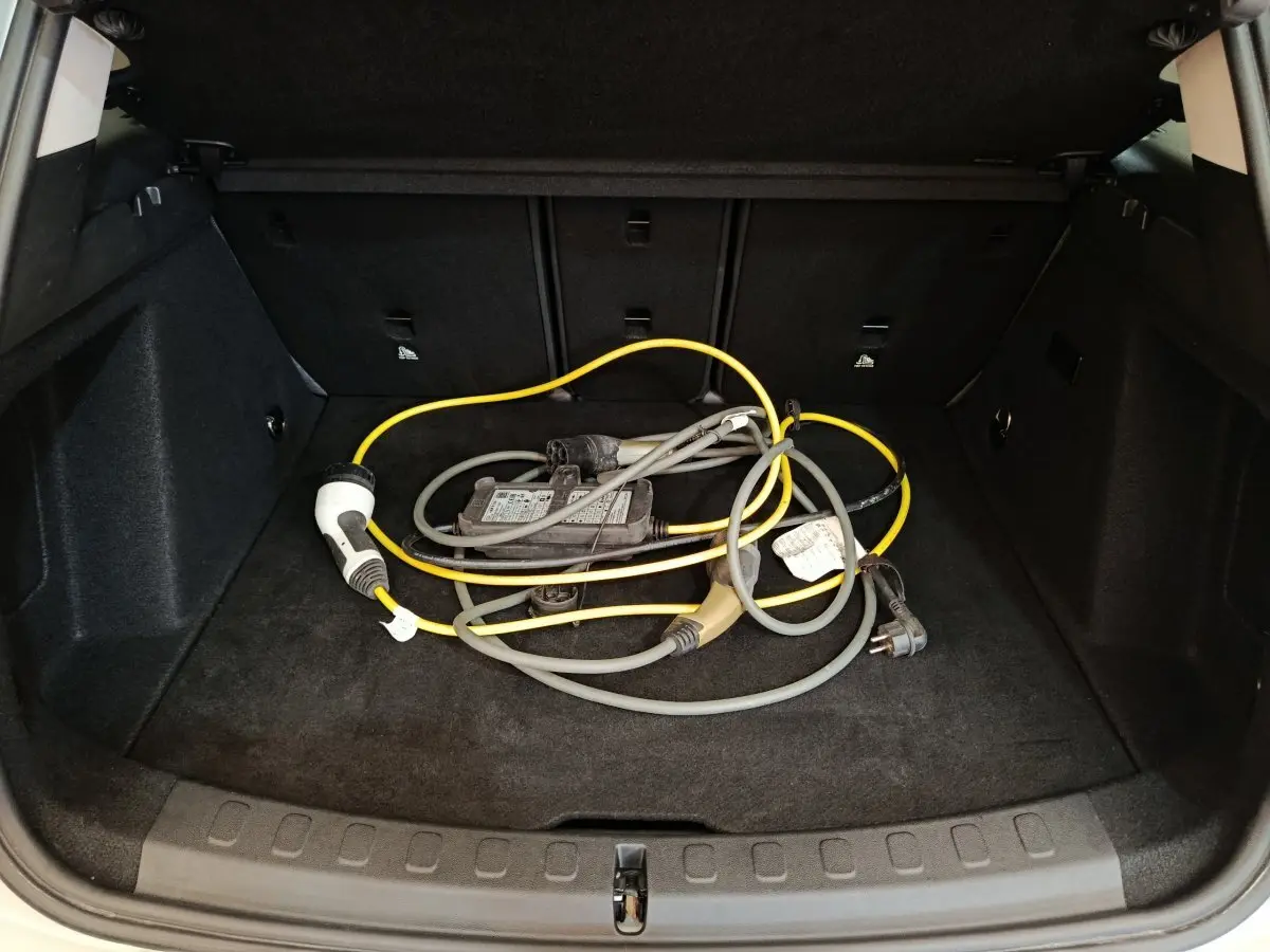 Coffre ouvert d'une MINI Countryman blanc, vue de l'arrière montrant un câble de recharge hybride posé au sol.