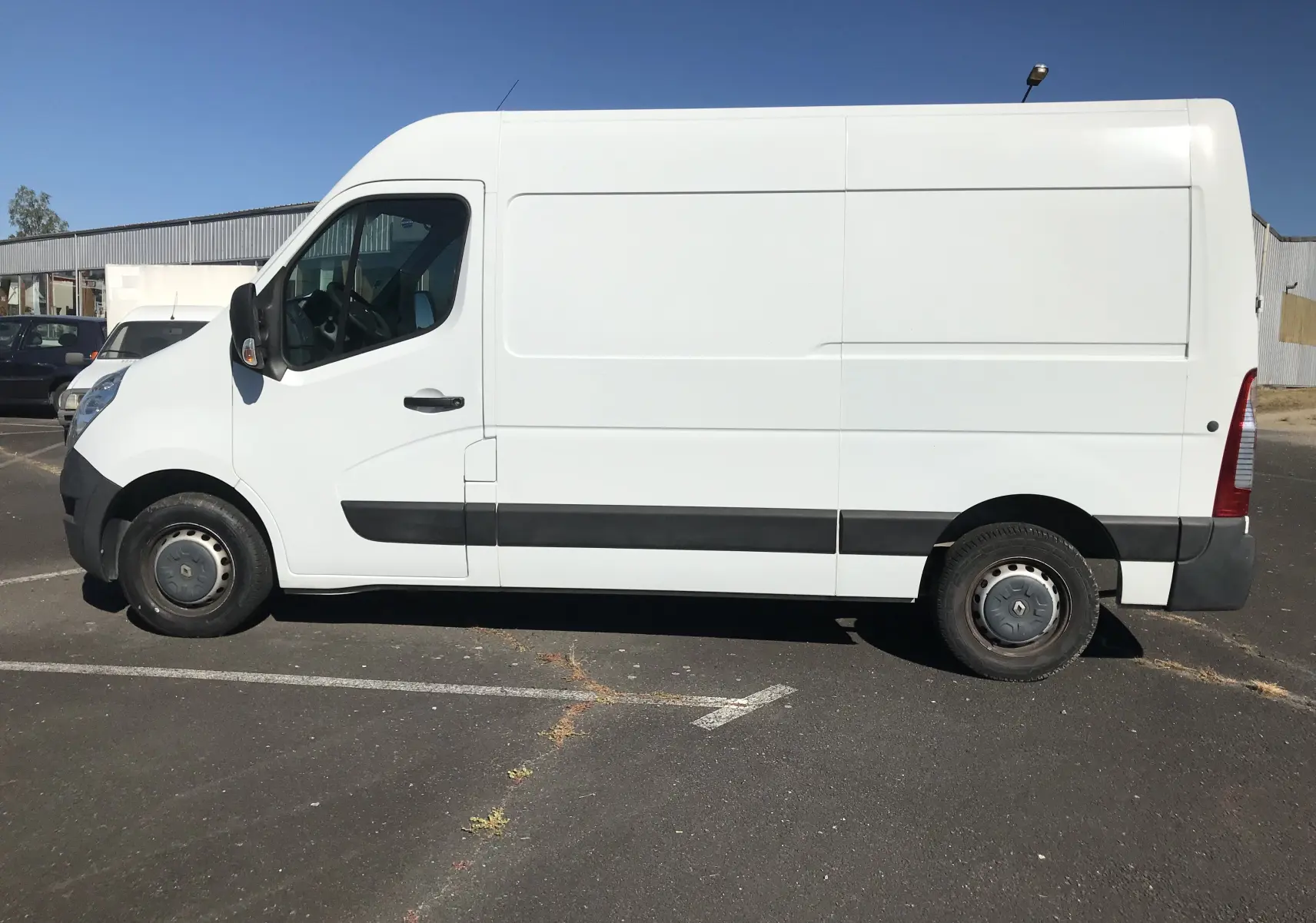 Vue latérale côté gauche d’un utilitaire Renault Master blanc avec bande noire sur le bas de caisse, stationné en extérieur.