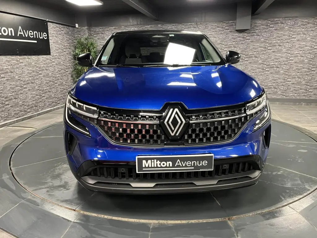 Vue frontale du Renault Austral bleu avec calandre à damier chrome sombre et logo Renault central lumineux.