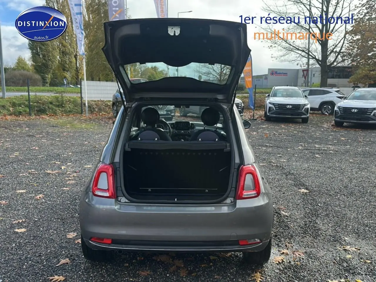 Vue arrière d'une Fiat 500 gris métallisé avec coffre ouvert sur un parking extérieur.