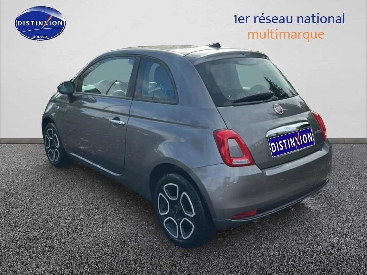 Fiat 500 gris vue 3/4 arrière droit, compacte avec jantes stylisées et feux arrière rectangulaires rouges.