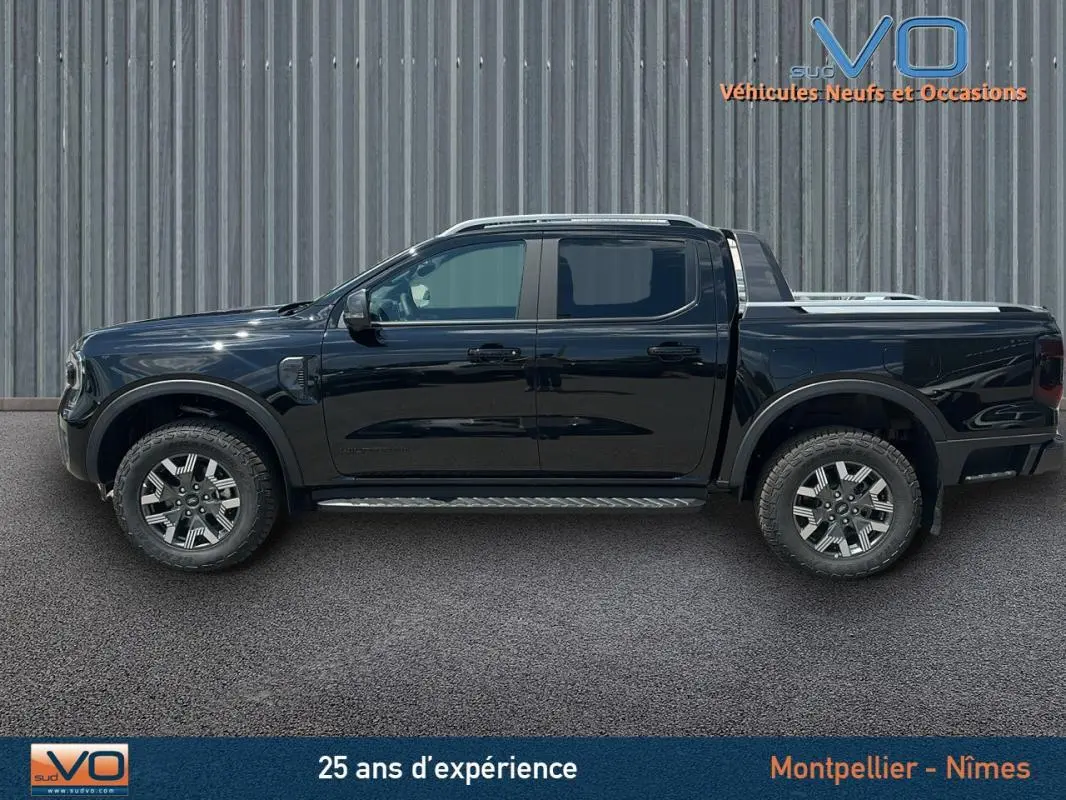 Profil côté gauche du Ford Ranger Wildtrak noir 2025 avec barres de toit, marchepieds et jantes alliage 18 pouces.