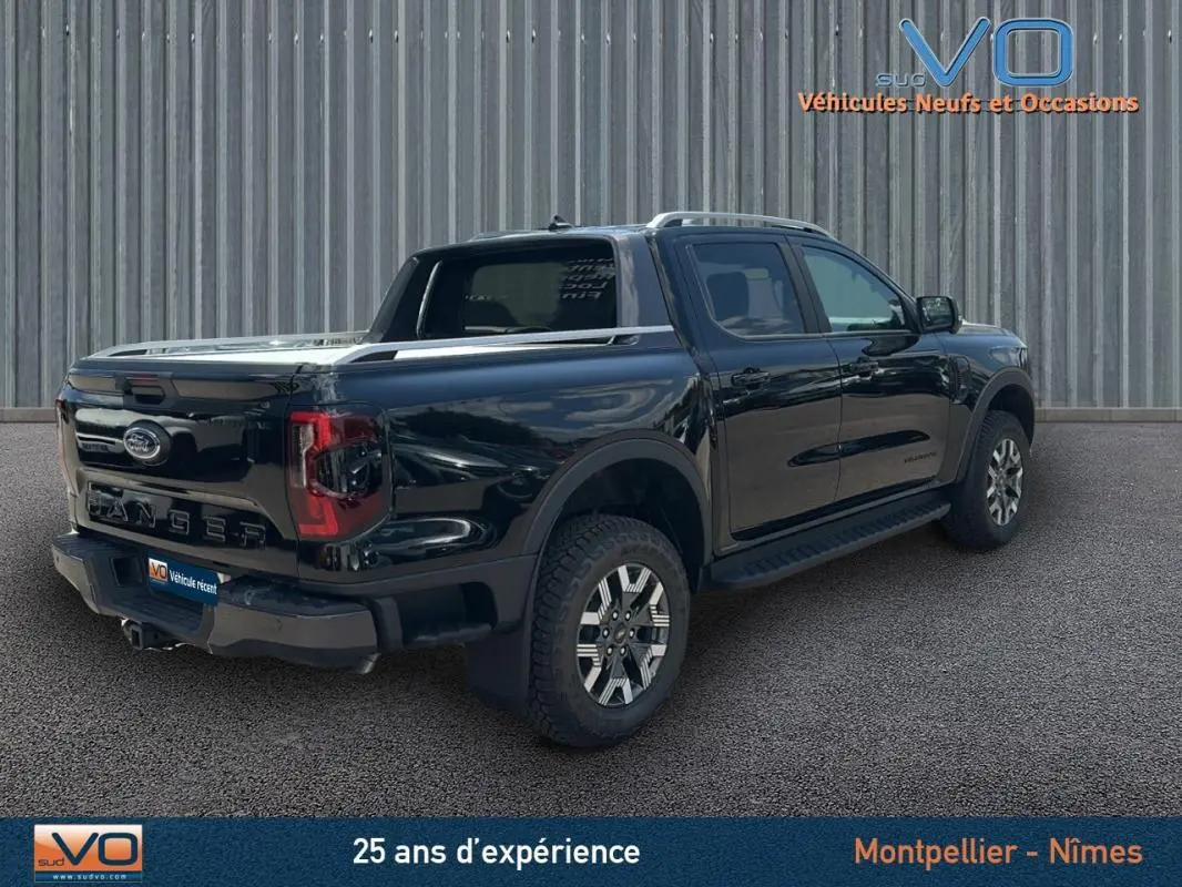 Ford Ranger Wildtrak noir en 3/4 arrière droit, avec barres de toit, marchepieds et jantes alliage 18 pouces.