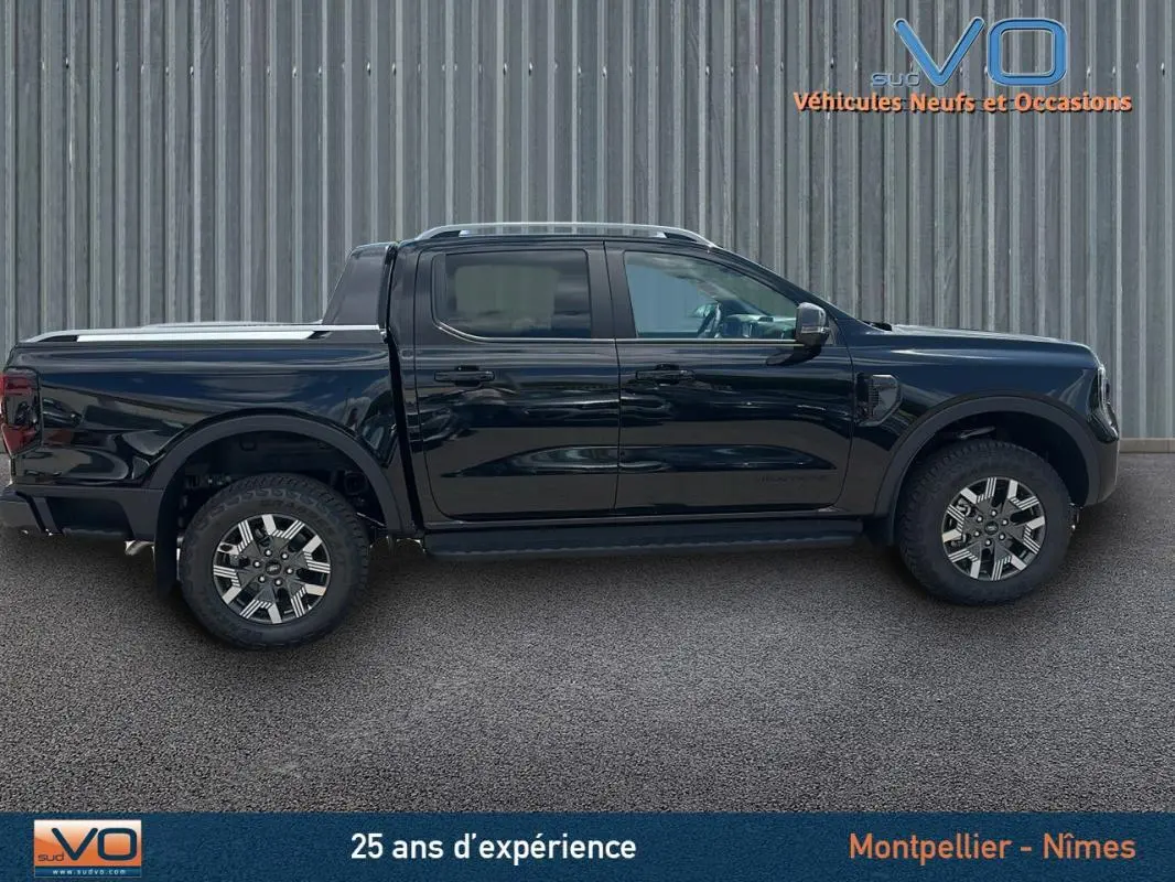 Profil côté droit du Ford Ranger Wildtrak 2025 noir avec double cabine, barres de toit et jantes alliage 18 pouces.