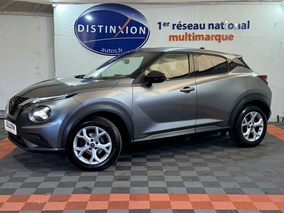 Profil droit d'un Nissan Juke gris clair 2021 dans un showroom avec logo Distinxion en arrière-plan.