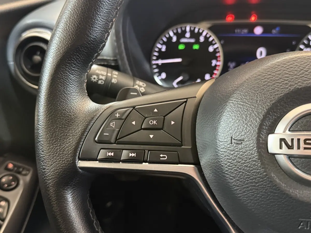 Gros plan sur le volant cuir noir du Nissan Juke 2021, avec commandes multifonctions et tableau de bord éclairé en arrière-plan.