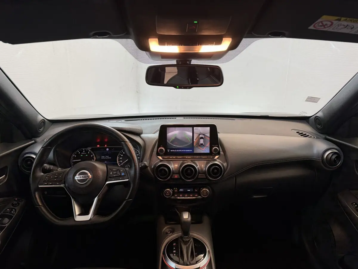 Vue intérieure avant du Nissan Juke gris clair 2021, tableau de bord avec écran tactile et volant cuir multifonctions.