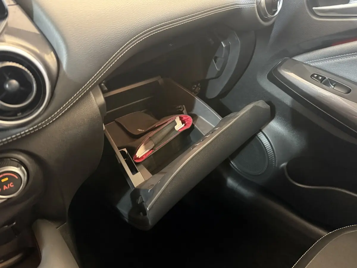 Gros plan sur la boîte à gants ouverte du Nissan Juke Tekna 2021, intérieur noir avec coutures blanches.