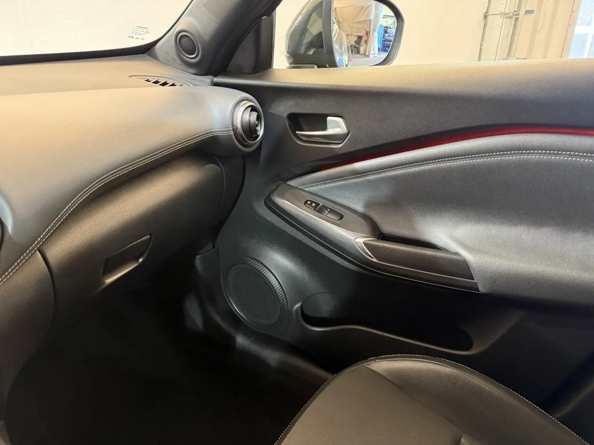Intérieur côté passager du Nissan Juke Tekna 2021, montrant la porte noire avec bande rouge et tableau de bord gris clair.