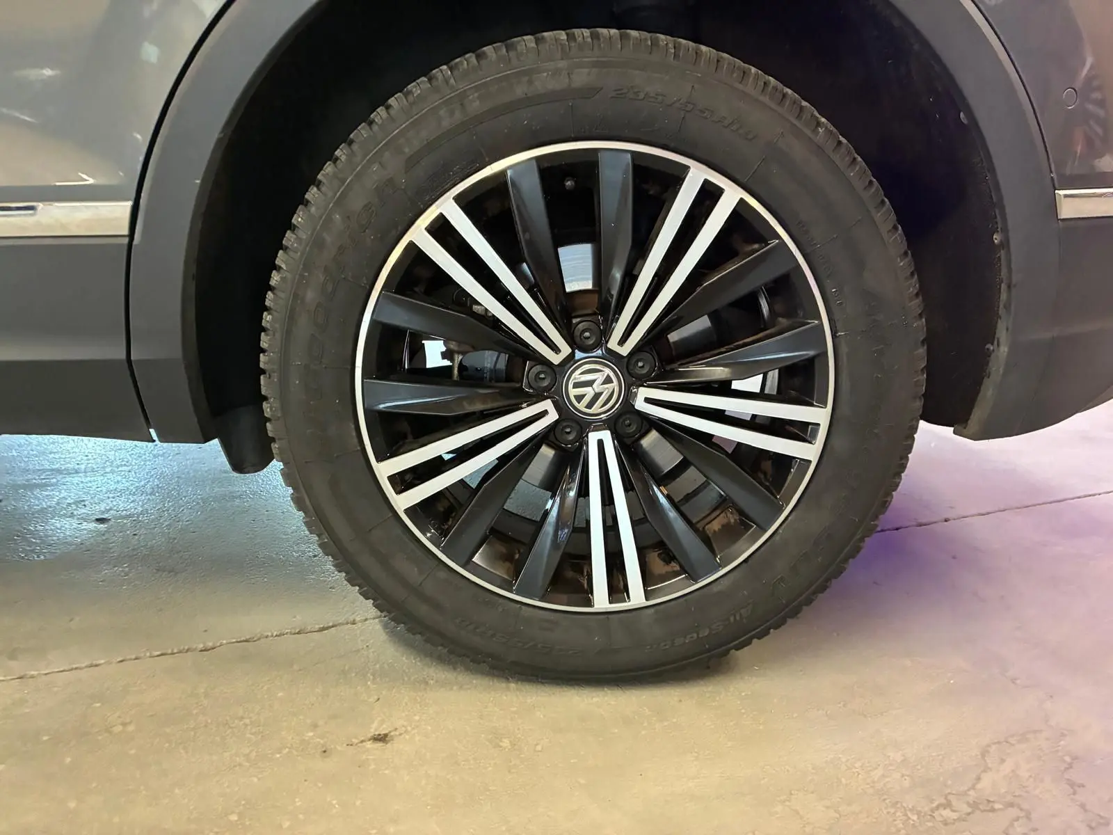 Gros plan sur la roue avant droite d'un Volkswagen Tiguan gris, mettant en valeur la jante alliage noire et argentée.